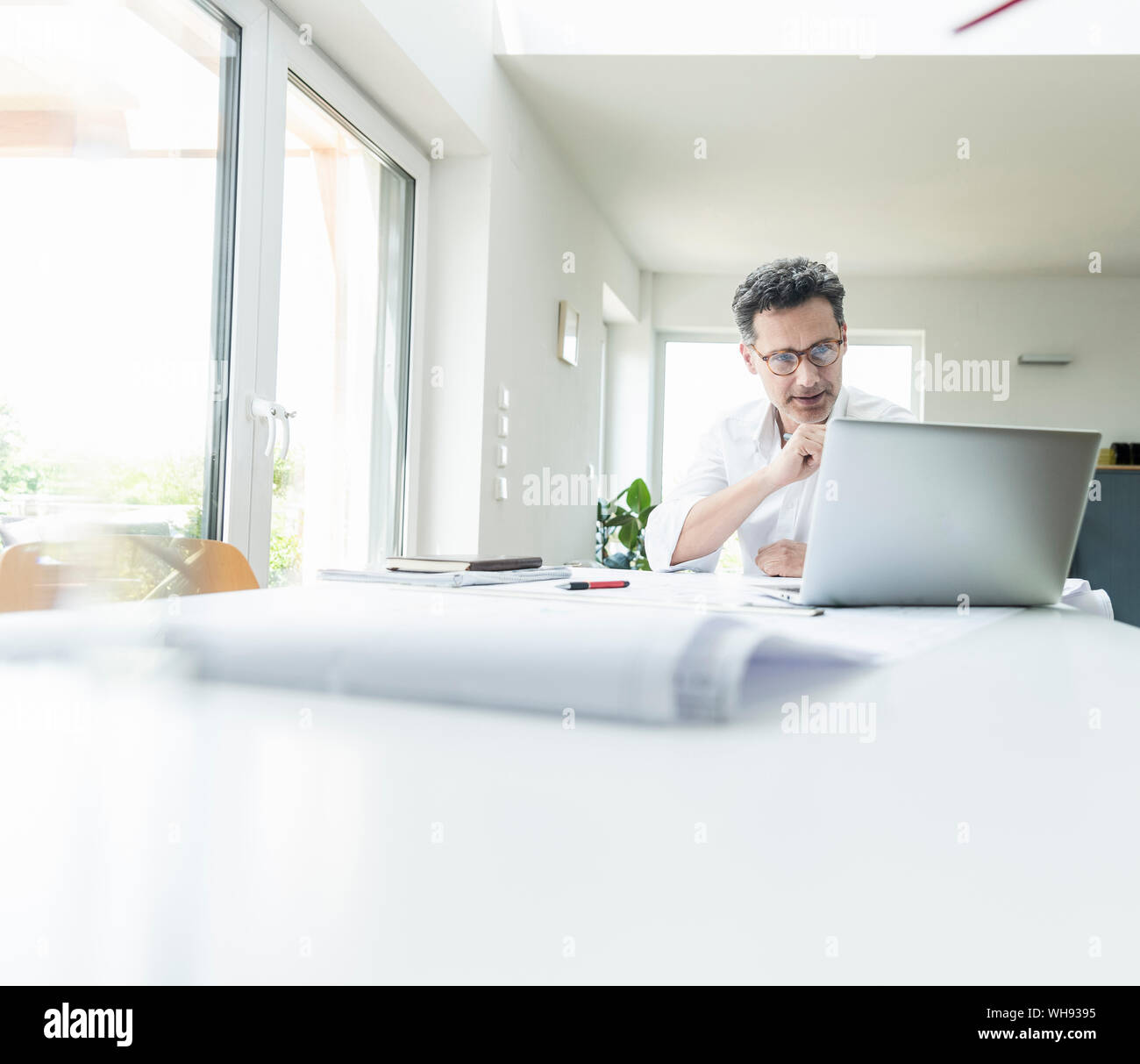 Assis dans le bureau de l'architecte lumineux, using laptop Banque D'Images