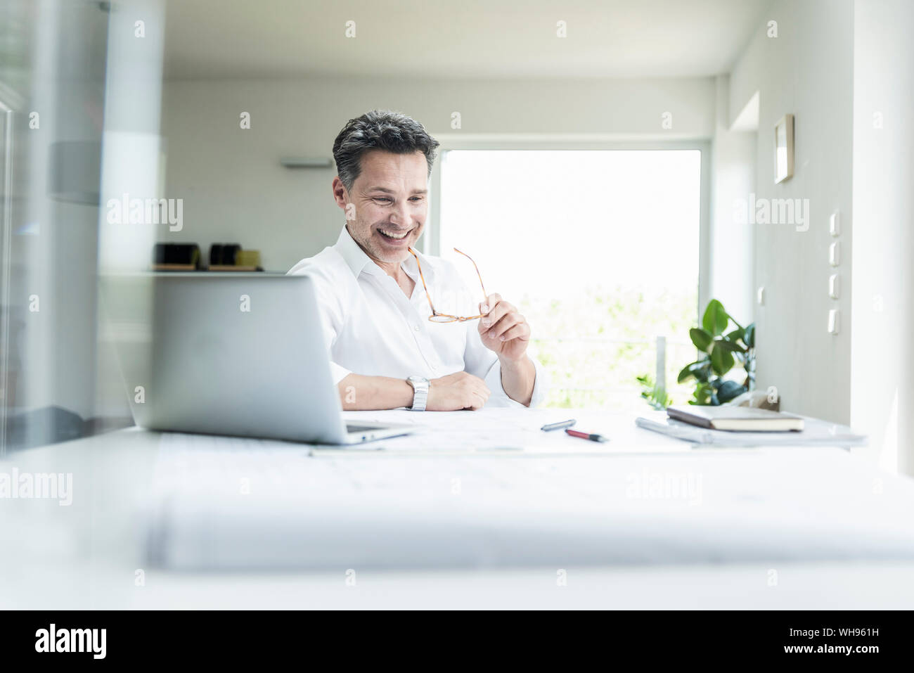 Assis dans le bureau de l'architecte lumineux, using laptop Banque D'Images