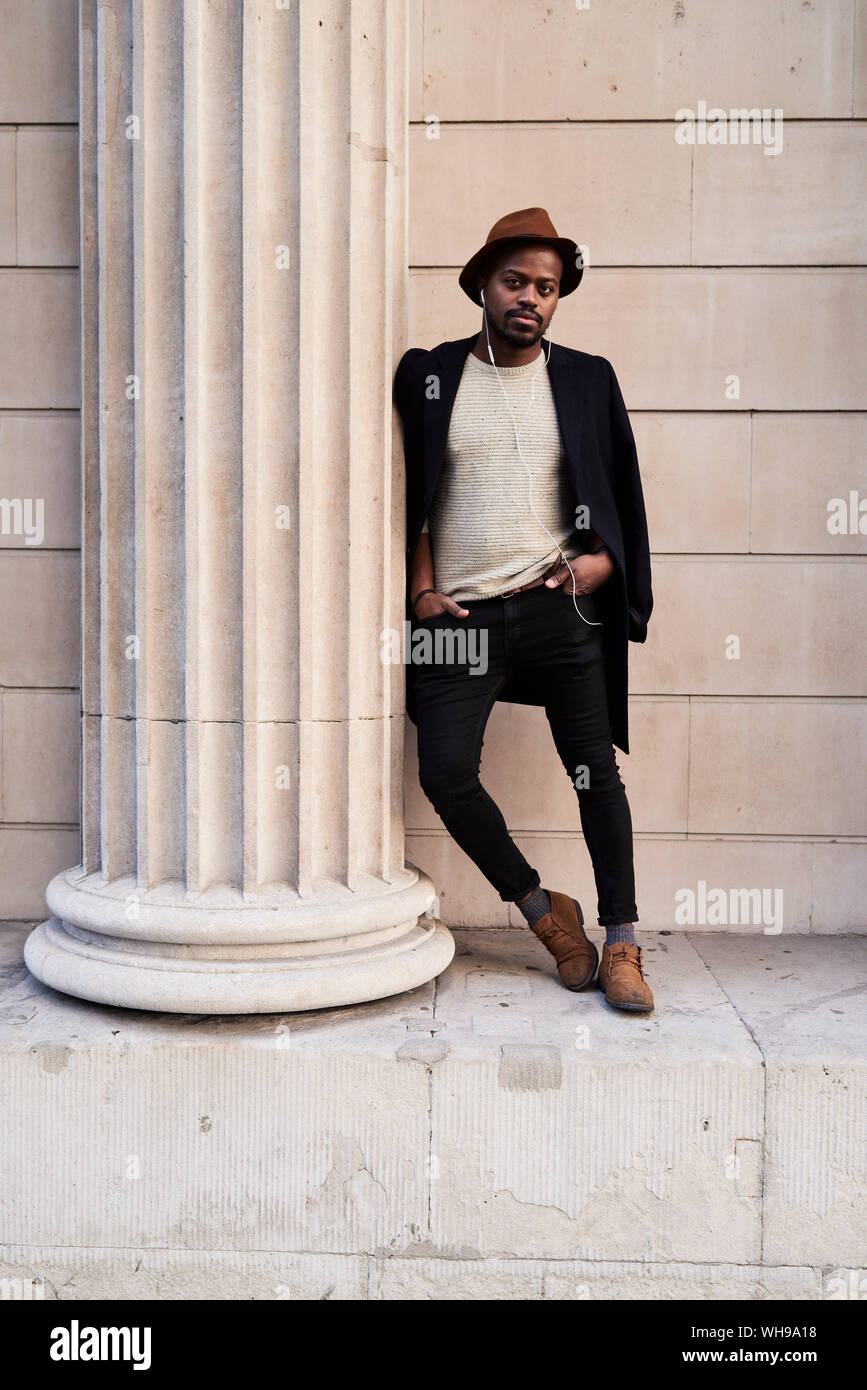 Mid adult man wearing chapeau brun, se penchant sur la colonne Banque D'Images