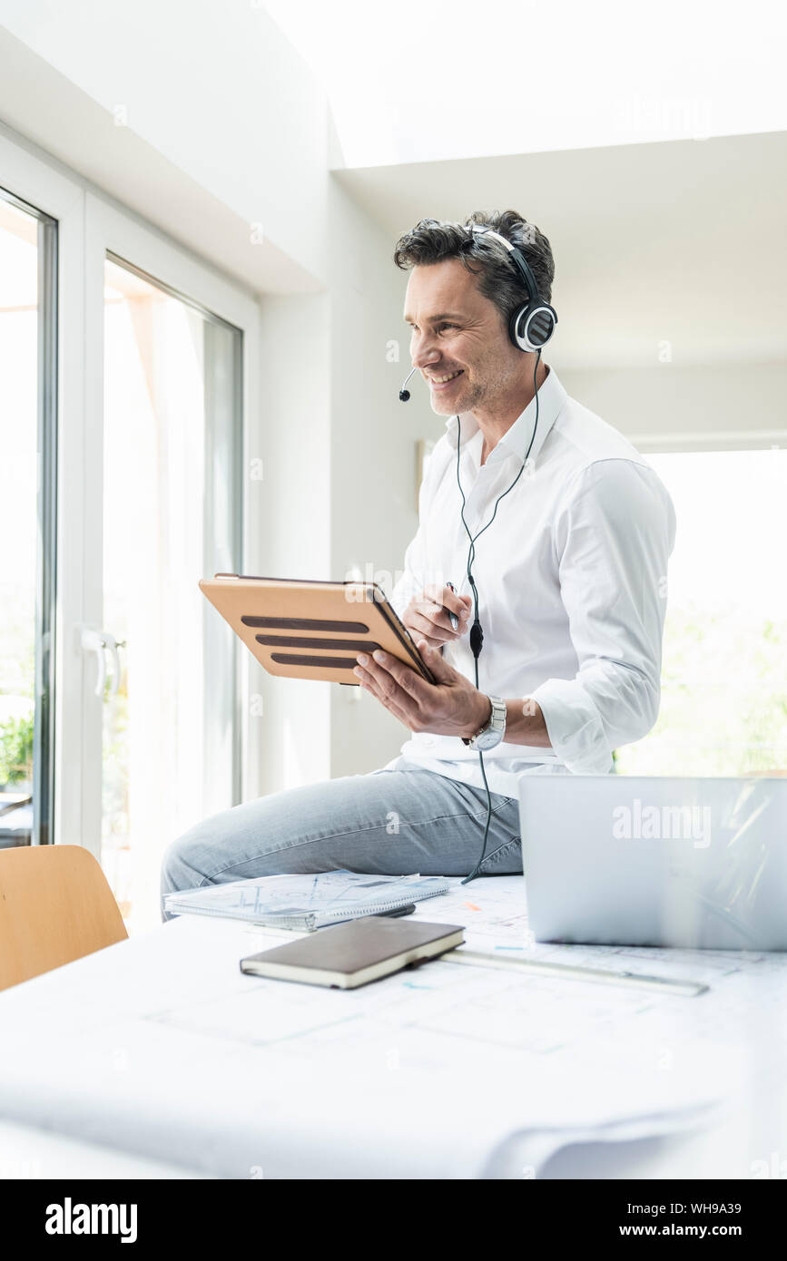 Businessman in bright office avoir conférence téléphonique, à l'aide du casque et digital tablet Banque D'Images