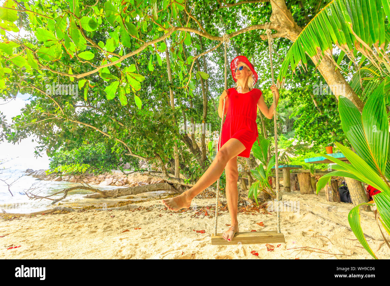 Femme en robe rouge touristiques swinging on tropical beach sous les cocotiers d'Anse sévère, La Digue, Seychelles, océan Indien, Afrique Banque D'Images