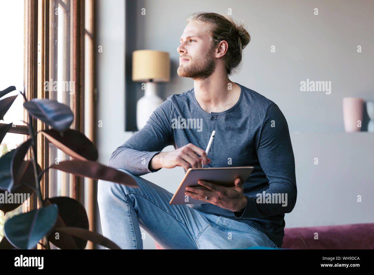 Jeune homme pensif à la maison avec une tablette numérique à la recherche d'une fenêtre Banque D'Images