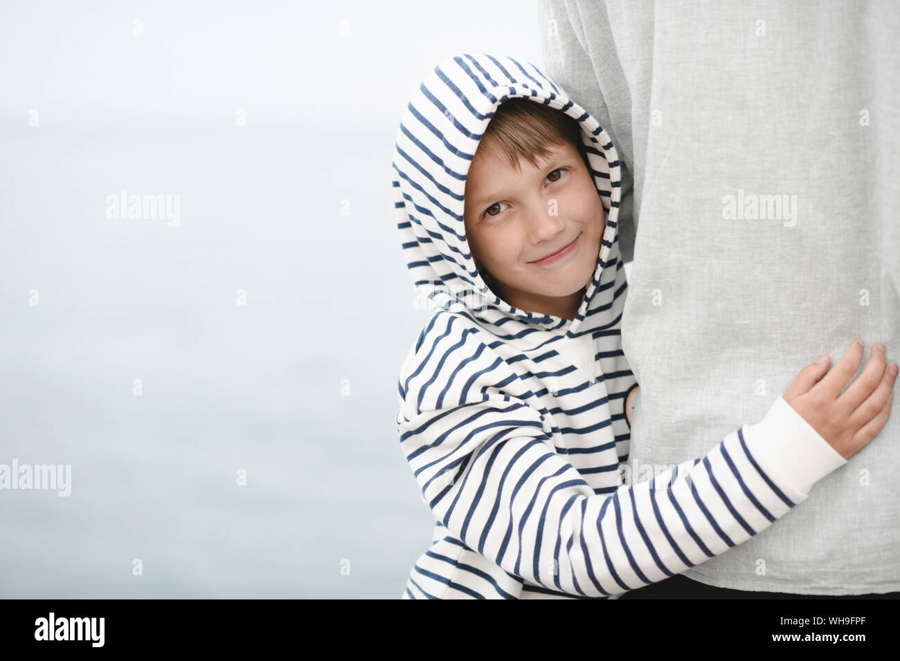 Portrait of smiling boy wearing striped Hooded Jacket hugging son père Banque D'Images