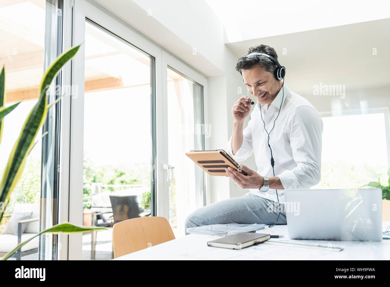 Businessman in bright office avoir conférence téléphonique, à l'aide du casque et digital tablet Banque D'Images
