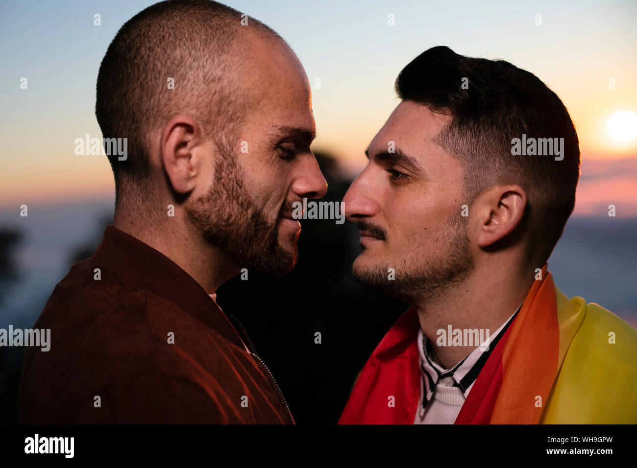 Couple gay avec Gay pride flag face à face au coucher du soleil Banque D'Images