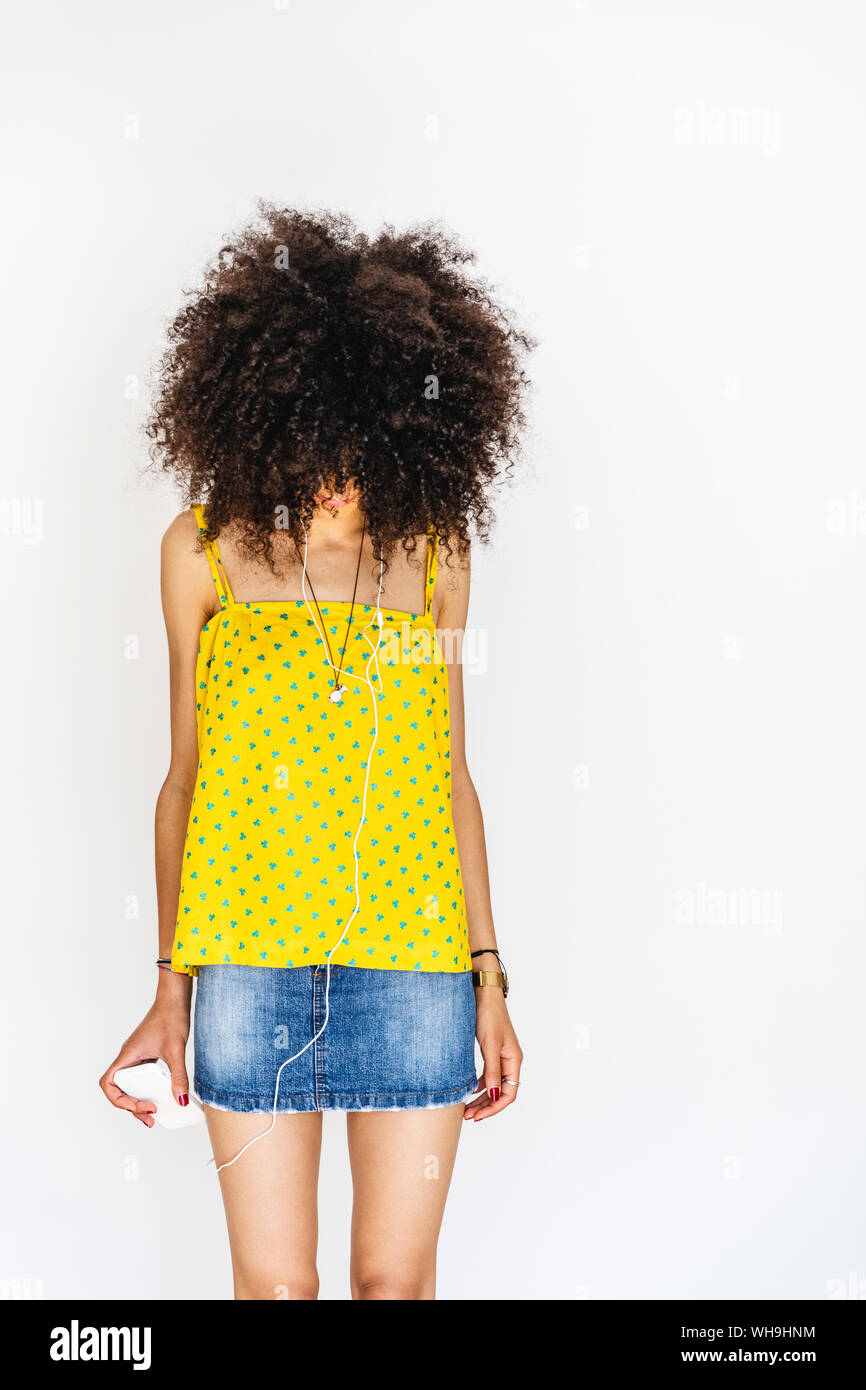 Jeune femme en utilisant son téléphone portable pour écouter de la musique, regardant vers le bas, fond blanc Banque D'Images