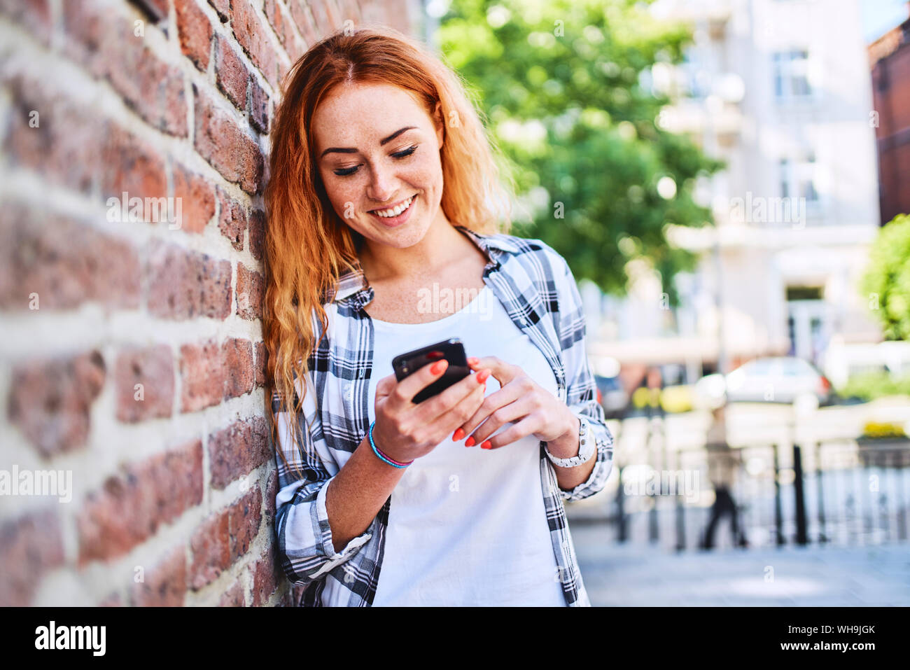 Jeune femme appuyée contre un mur de briques dans la ville lors de l'utilisation de smartphone Blackberry Banque D'Images