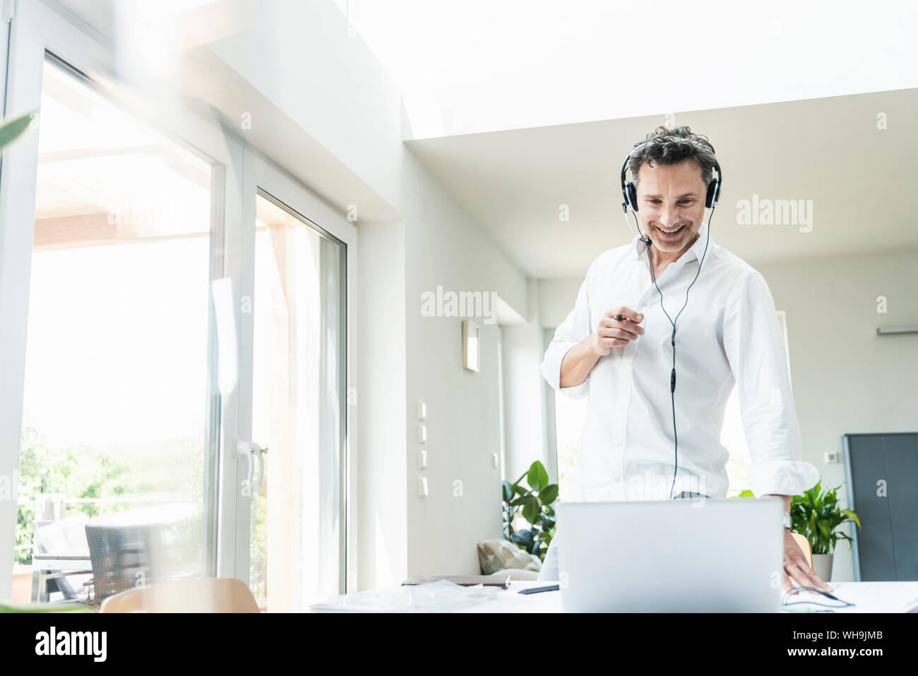Businessman in bright office avoir conférence téléphonique, à l'aide du casque et l'ordinateur portable Banque D'Images