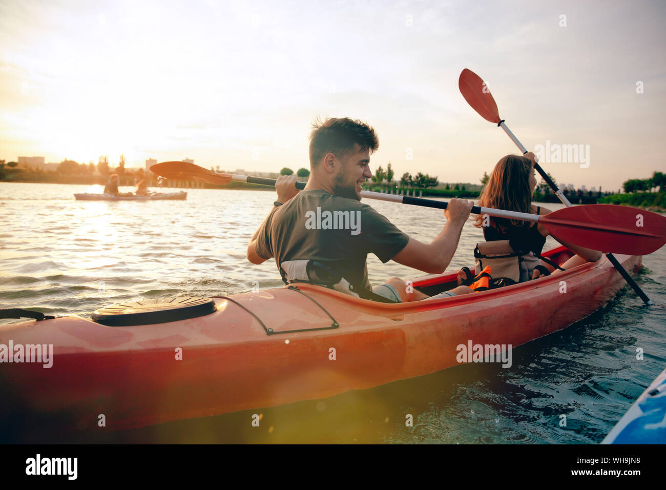 Certain young caucasian couple kayak sur rivière avec coucher du soleil dans l'arrière-plan. Avoir du plaisir dans l'activité de loisirs. Romantique et heureux homme et femme sur le kayak. Le sport, les relations concept. Banque D'Images