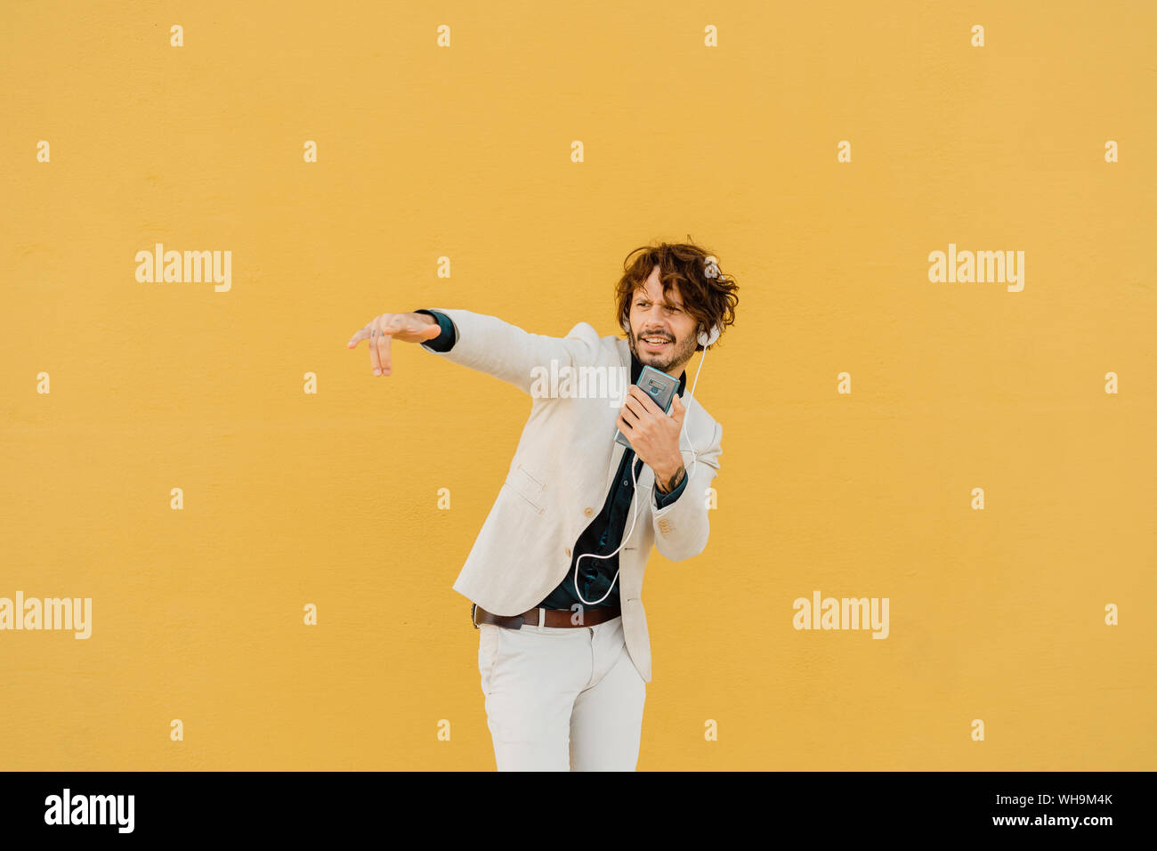 Businessman chante et danse en face de mur jaune à l'écoute de la musique avec des écouteurs et smartphone Banque D'Images