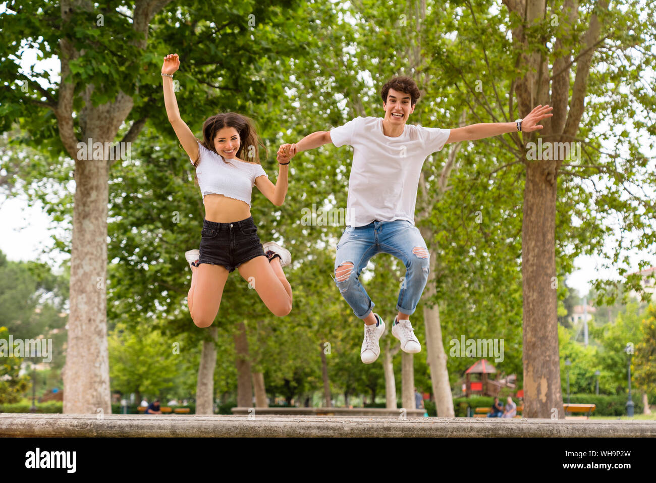 Jeune couple sautant d'un mur dans le parc Banque D'Images