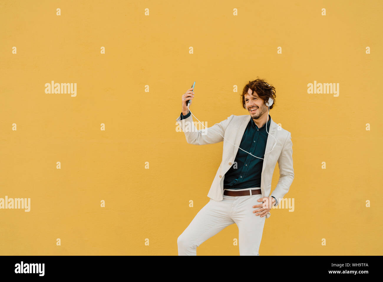 Businessman danser devant mur jaune à l'écoute de la musique avec des écouteurs et smartphone Banque D'Images