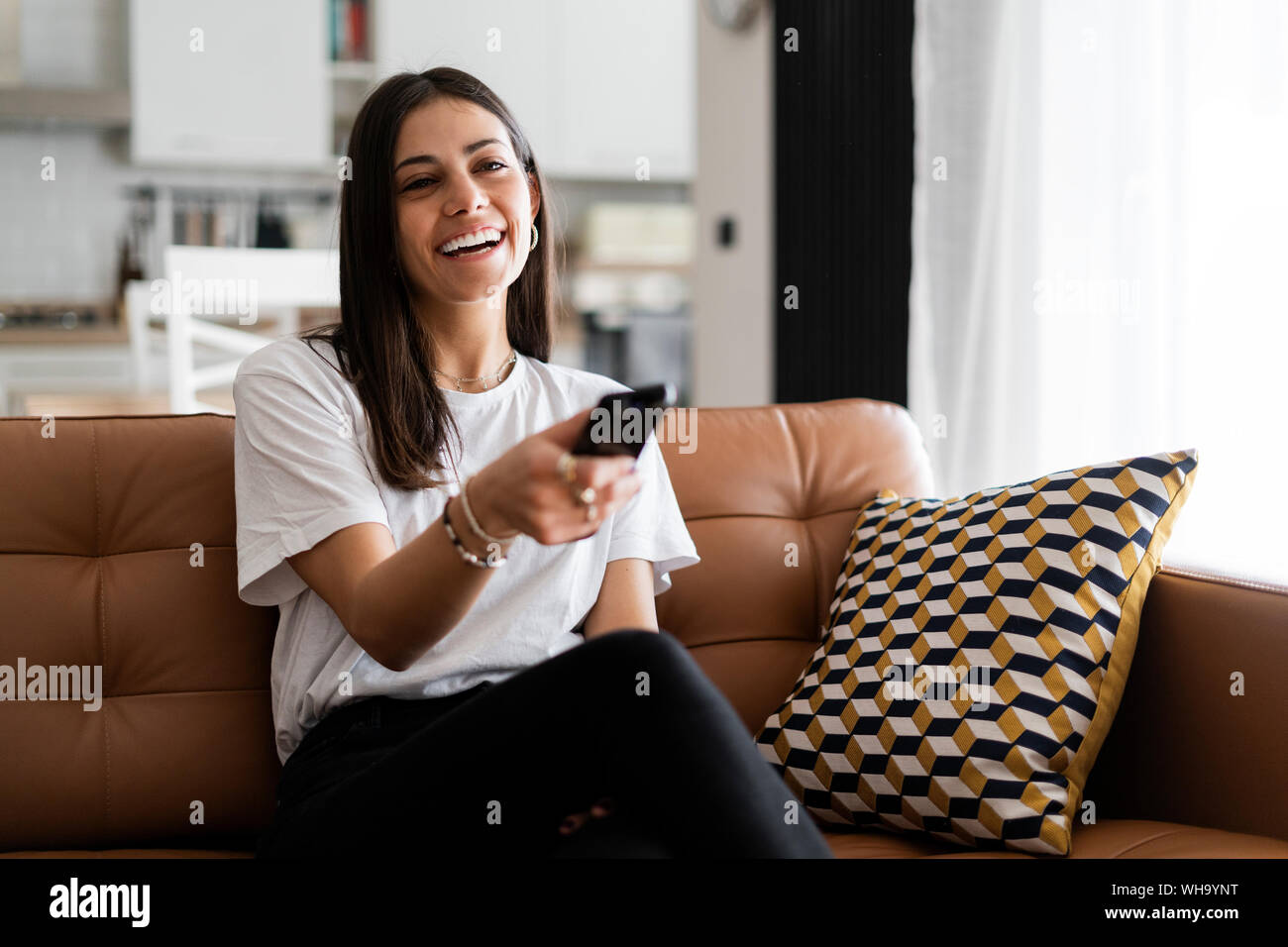 Happy young woman sitting on couch à la maison regarder la télévision Banque D'Images