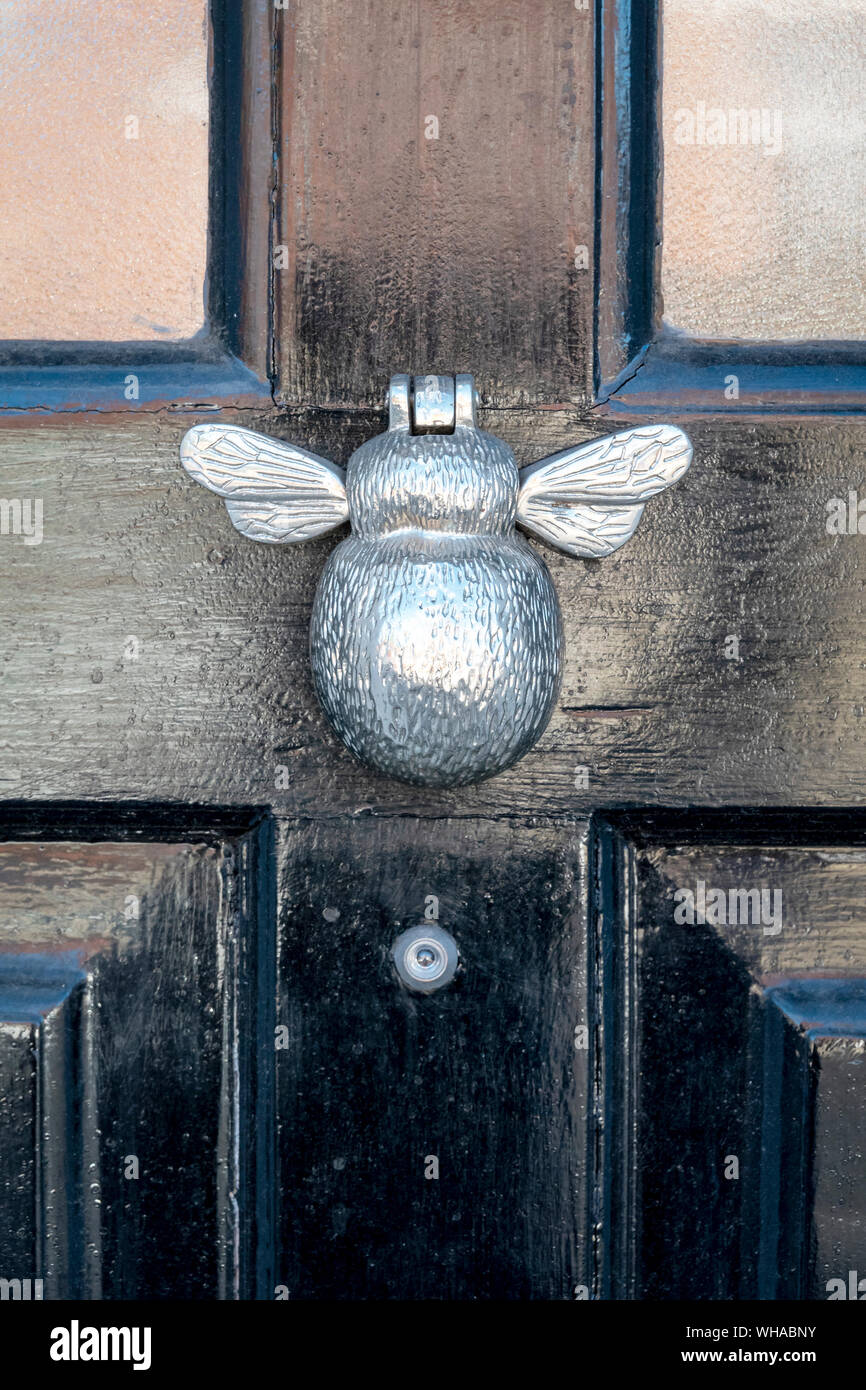 Heurtoir de porte en métal brillant dans la forme d'un insecte ailé sur une porte peinte en noir avec lentille trou espion ci-dessous Banque D'Images