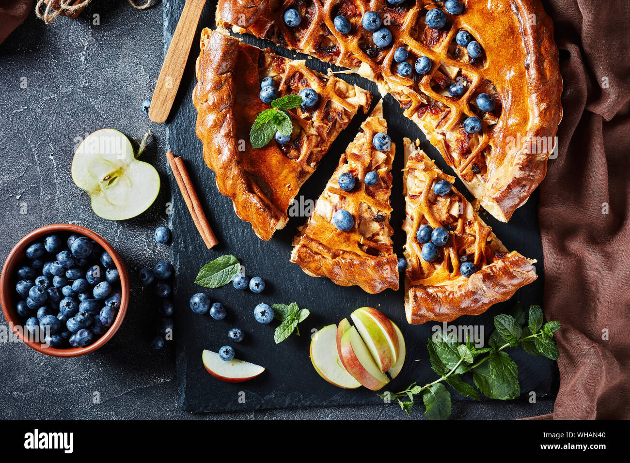 Close-up composé de délicieuses tranches de pomme Tarte aux bleuets sur un plateau en ardoise noire sur une table en béton avec des ingrédients à l'arrière-plan, horizontal vie Banque D'Images