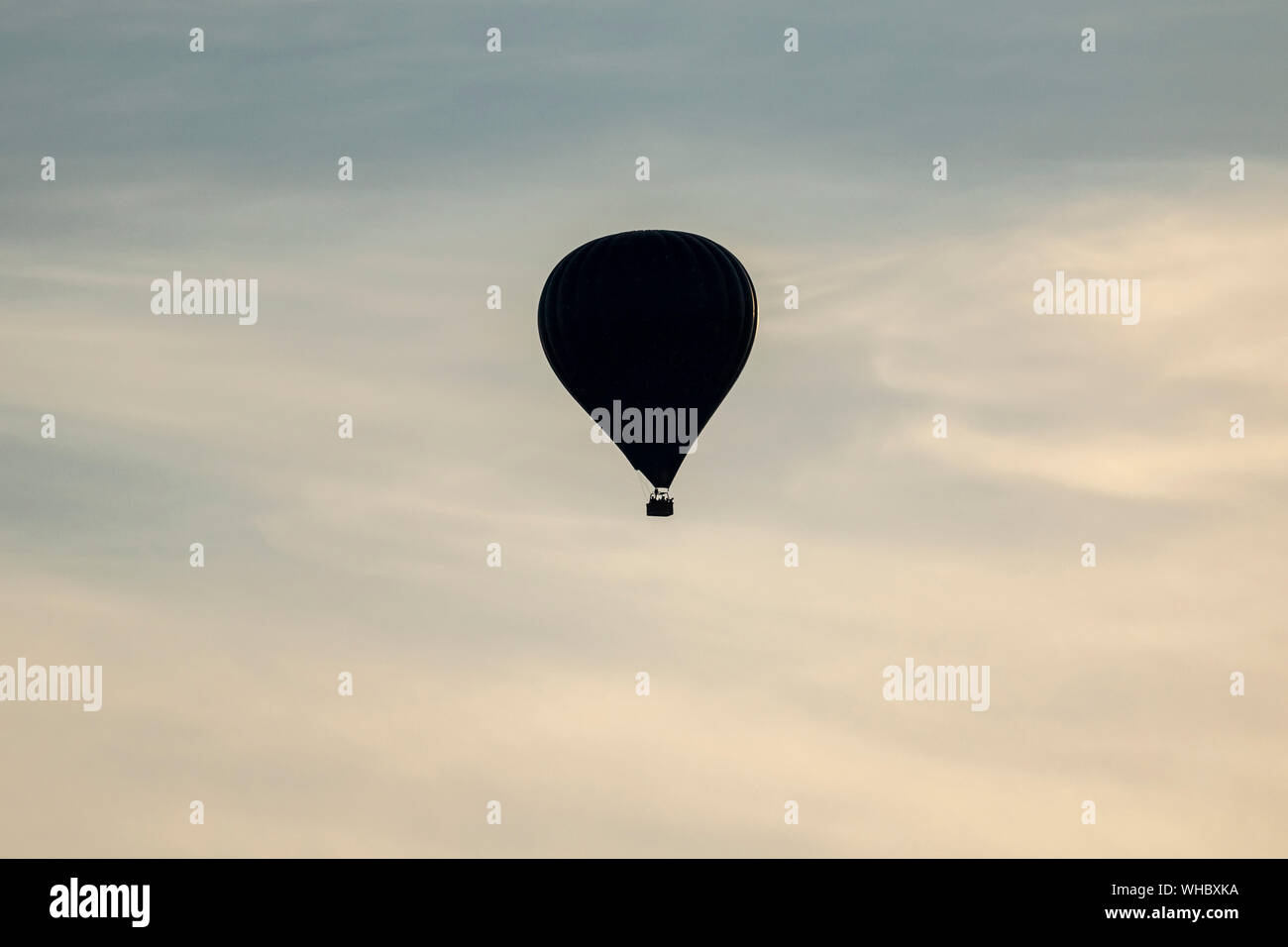 Un portrait d'une silhouette d'un ballon à air chaud dans un ciel nuageux bleu rempli de lumière du coucher du soleil à venir. Banque D'Images