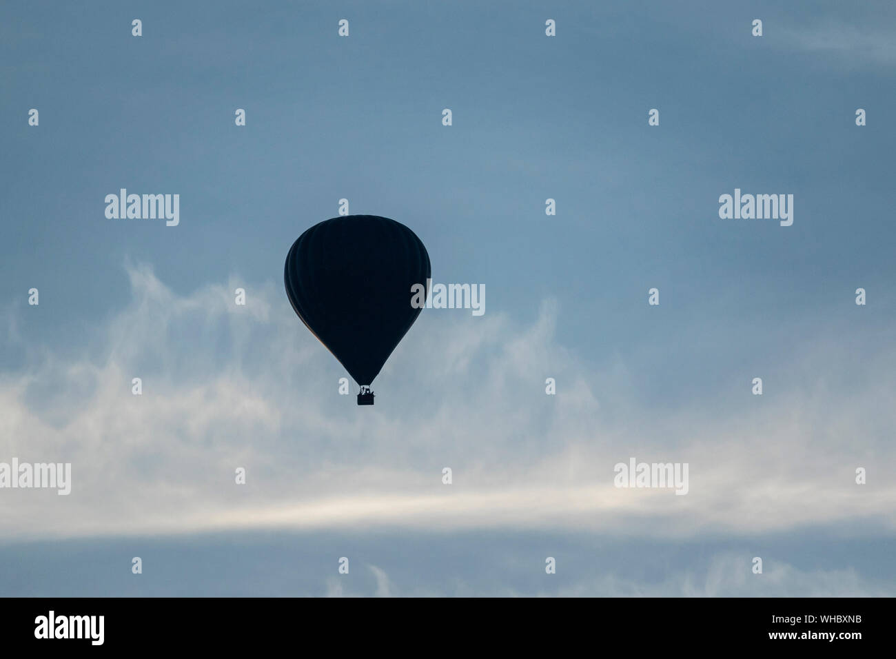 Un portrait d'un ballon à air chaud au loin, flottant dans un ciel bleu avec quelques nuages voile. Banque D'Images