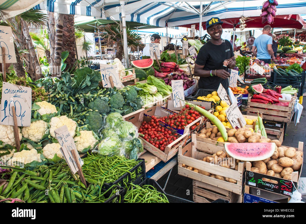 A smiling vendeur se dresse, fraîches, les légumes locaux au marché plein air sur un été à Ortigia, Sicile Banque D'Images