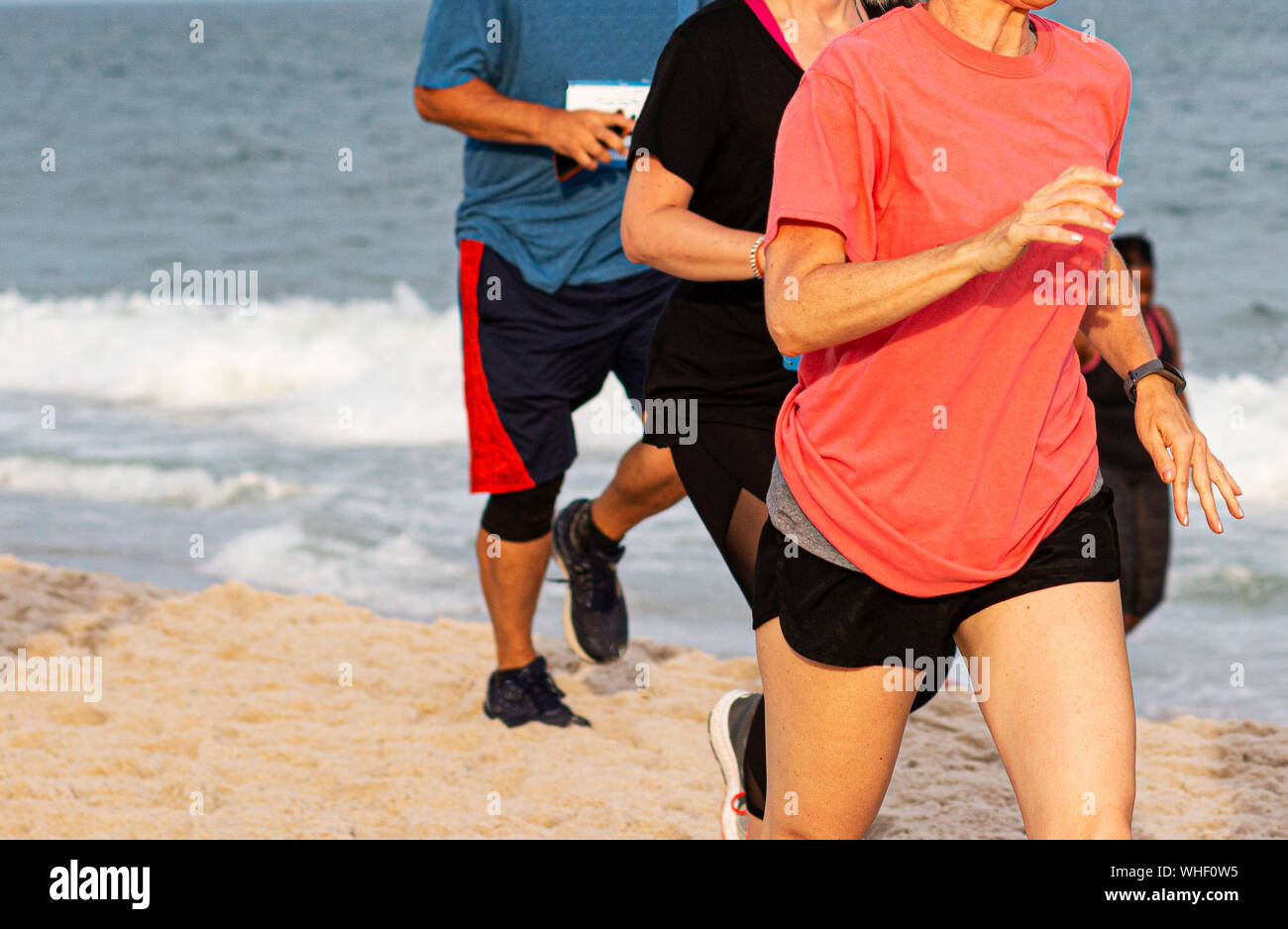 Les personnes en cours d'exécution du sable par l'océan sur une plage de Long Island. Banque D'Images