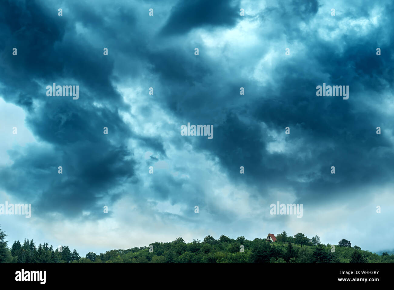 Ciel d'orage au-dessus de la maison dans la forêt sur une colline sous les nuages de pluie spectaculaire Banque D'Images