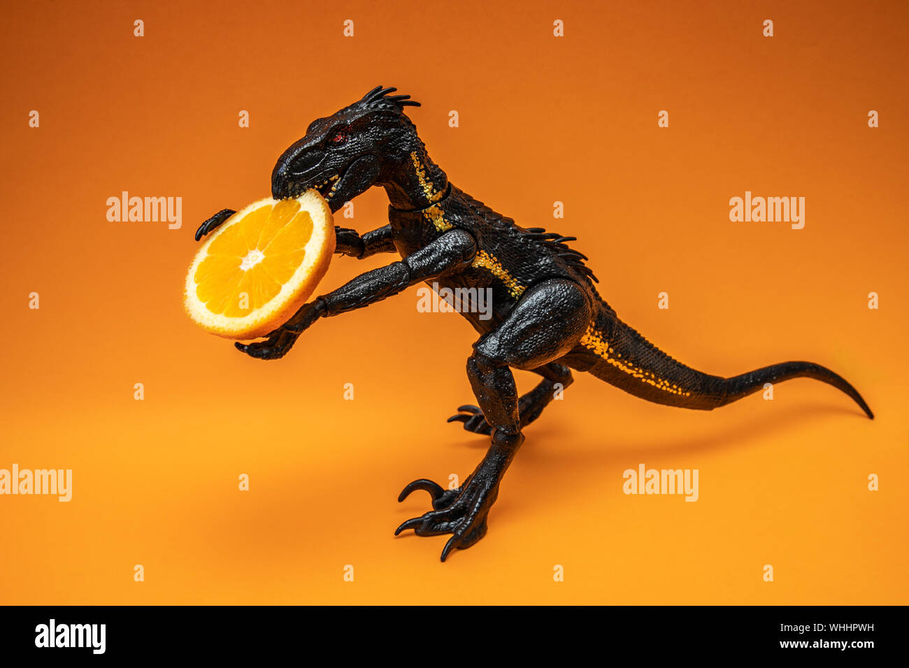 Dinosaure noir avec tranche de lime, isolé sur fond orange, copier du texte ou de l'espace pour la conception de la frontière Banque D'Images