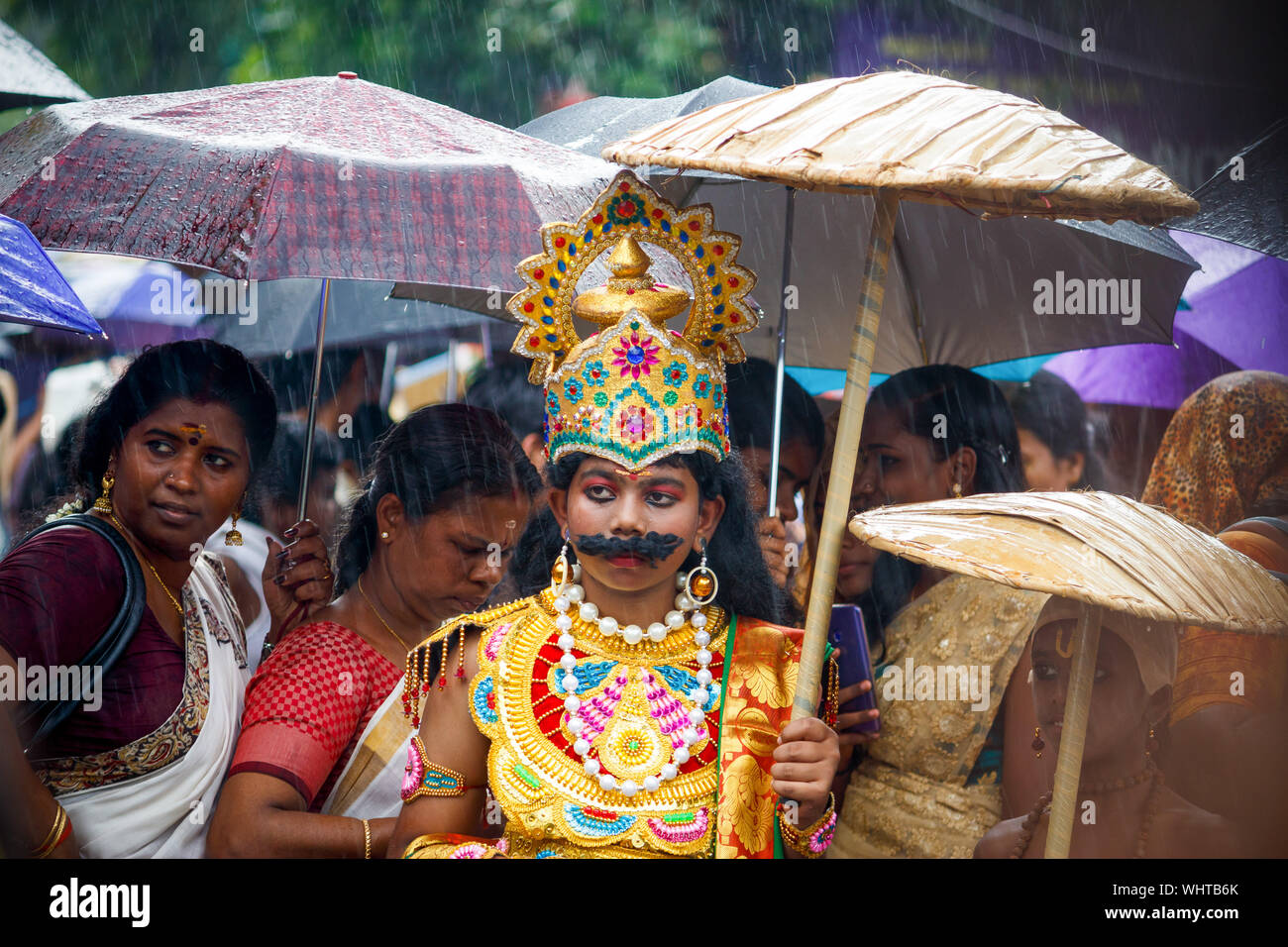 Kochi, Kerala State, India - 2 septembre 2019 - Personne habillé comme Mahabali debout dans la pluie avec des feuilles traditionnelles au cours de Athachamayam parapluie Banque D'Images