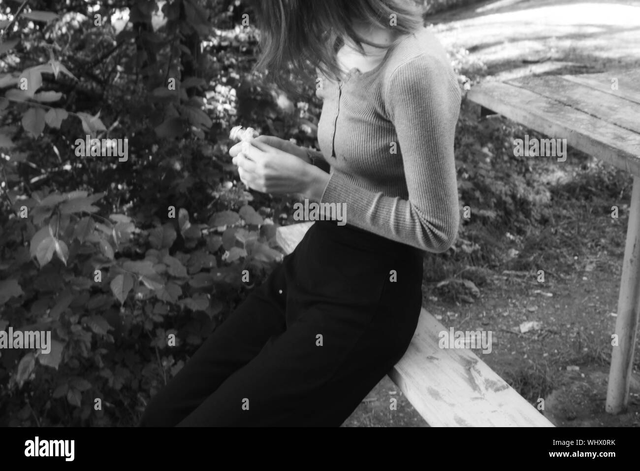 Prise de vue en niveaux de gris d'une femme seule assise sur un banc dans un jardin et tenant une fleur dans ses mains Banque D'Images