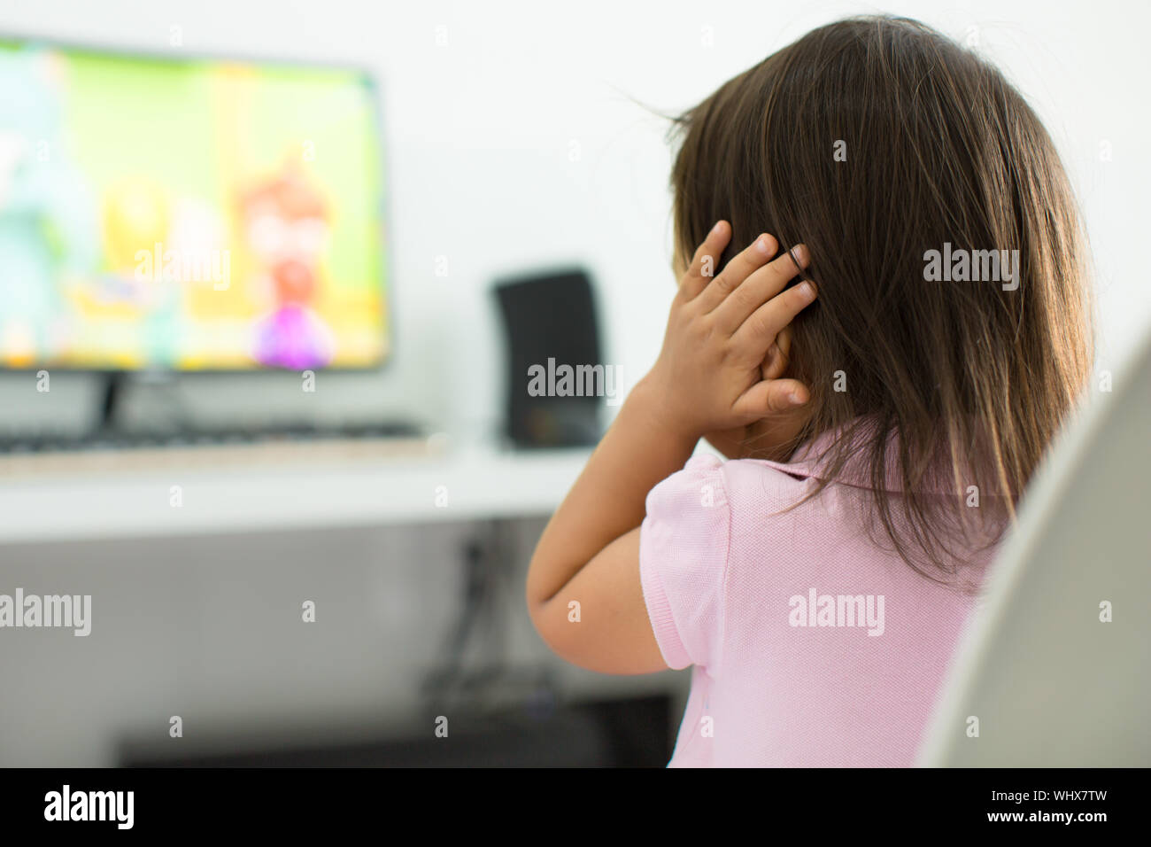 Un enfant regardant la TV maintenant ses oreilles parce qu'elle a peur du son ; le comportement de l'enfant thème Banque D'Images