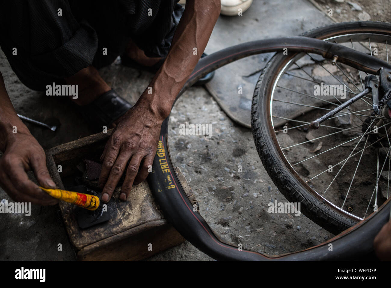 Un homme de réparation de vélos la fixation d'un pneu à plat sur un vélo sur une fin d'après-midi dans le nord de l'Inde. Banque D'Images