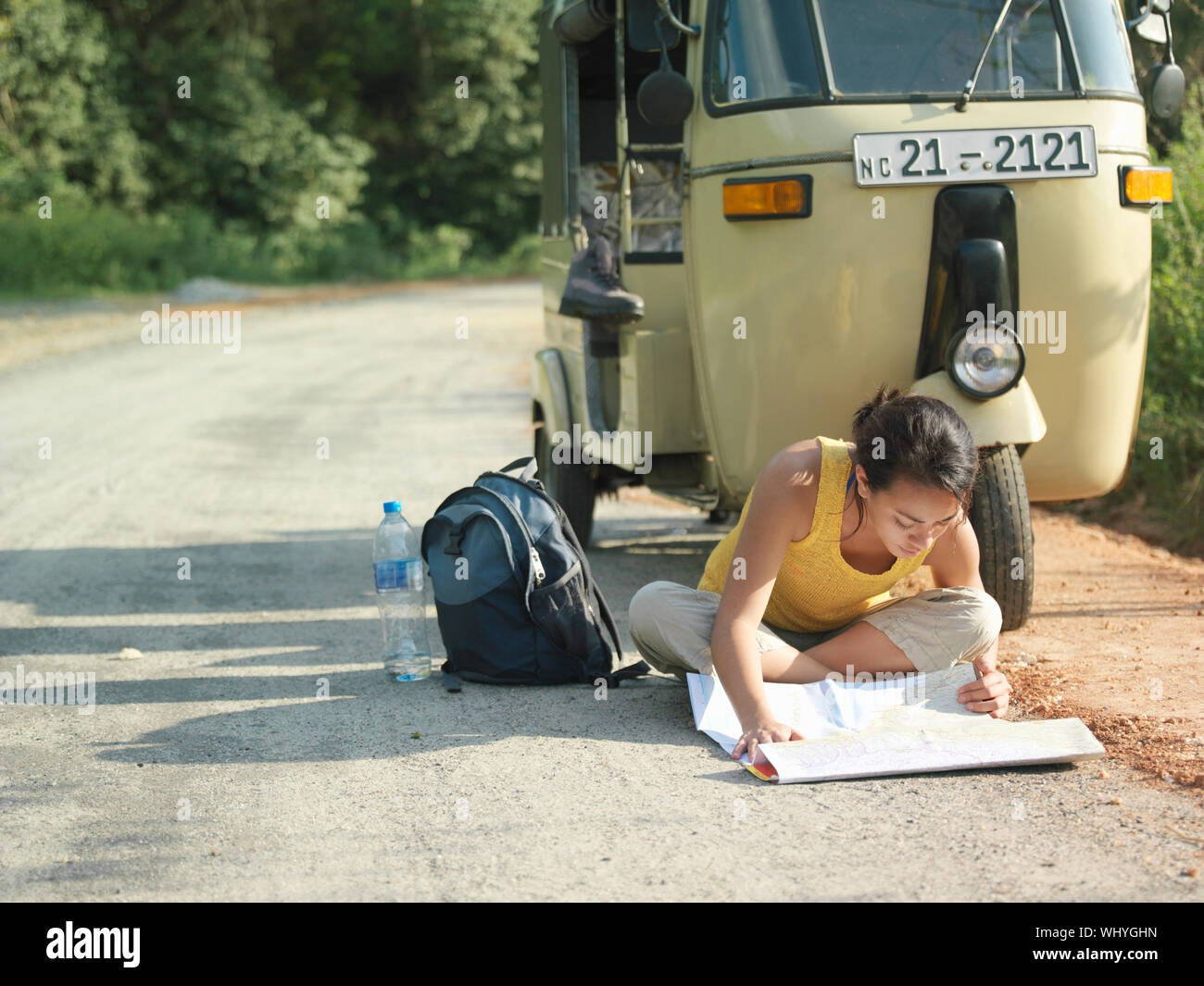 Young mixed race woman sitting cross legged on country road et la lecture de carte en auto rickshaw Banque D'Images