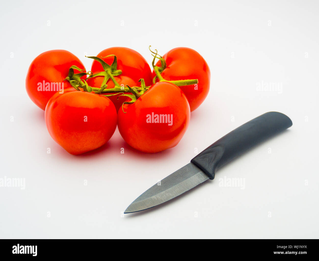 Les tomates rouges frais et un couteau en céramique noir isolé sur fond blanc. Banque D'Images