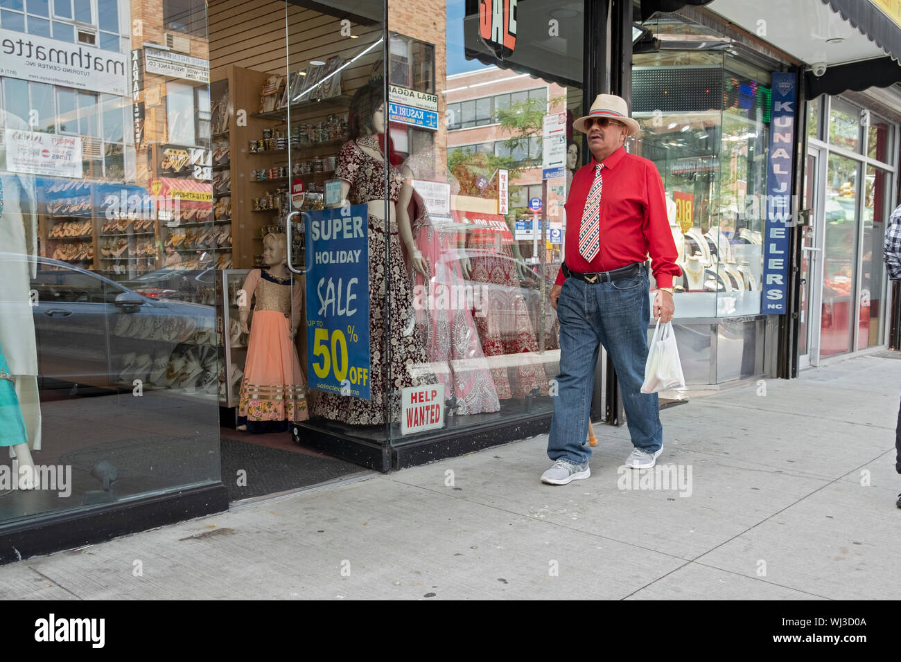 Un homme en chemise rouge vif d'un sari promenades en boutique sur 74e Rue à la très grande diversité Jackson Heights, Queens, New York. Banque D'Images