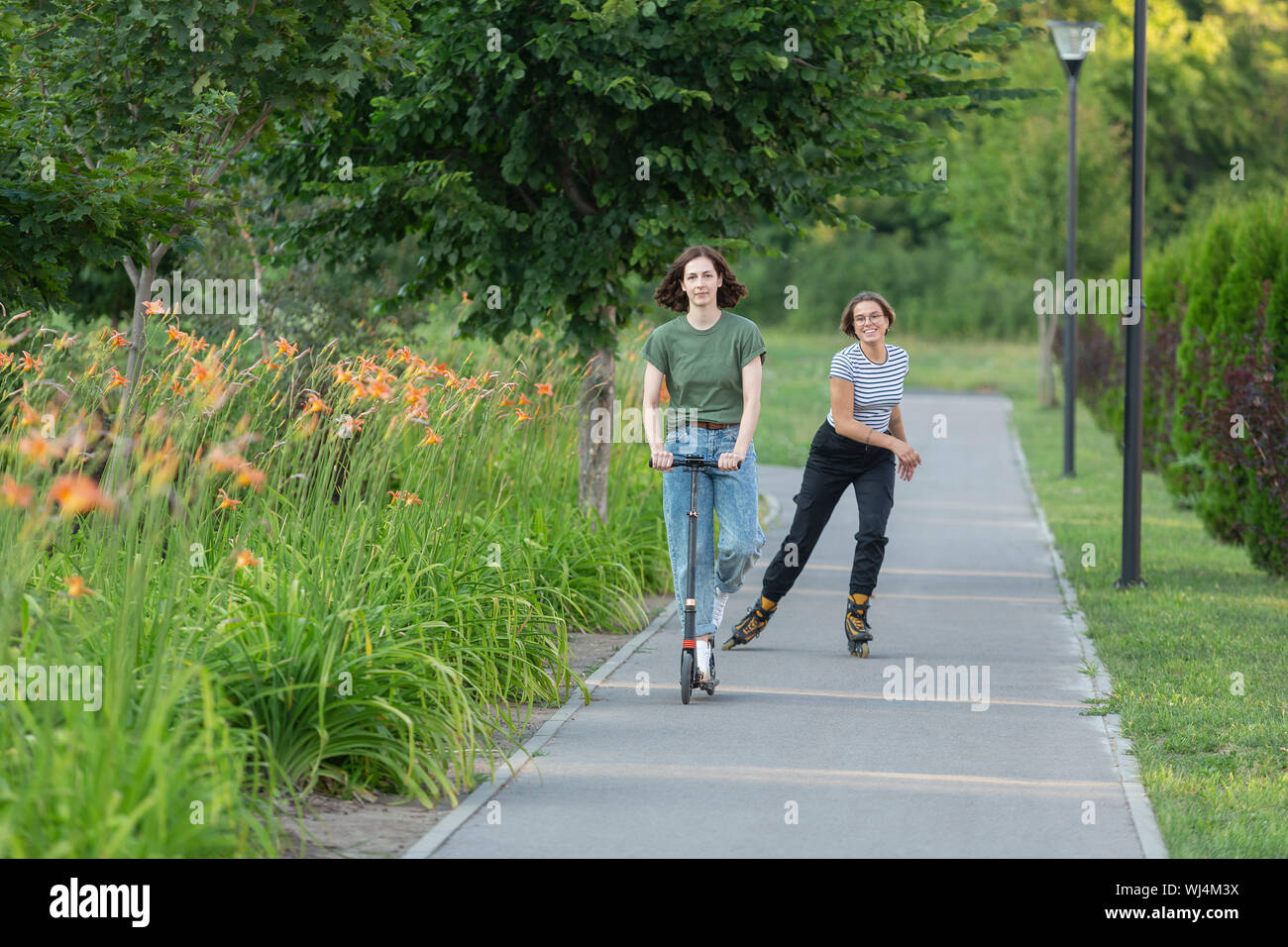Le patin à roues alignées et les femmes équitation pousser scooter sur sentier du parc Banque D'Images