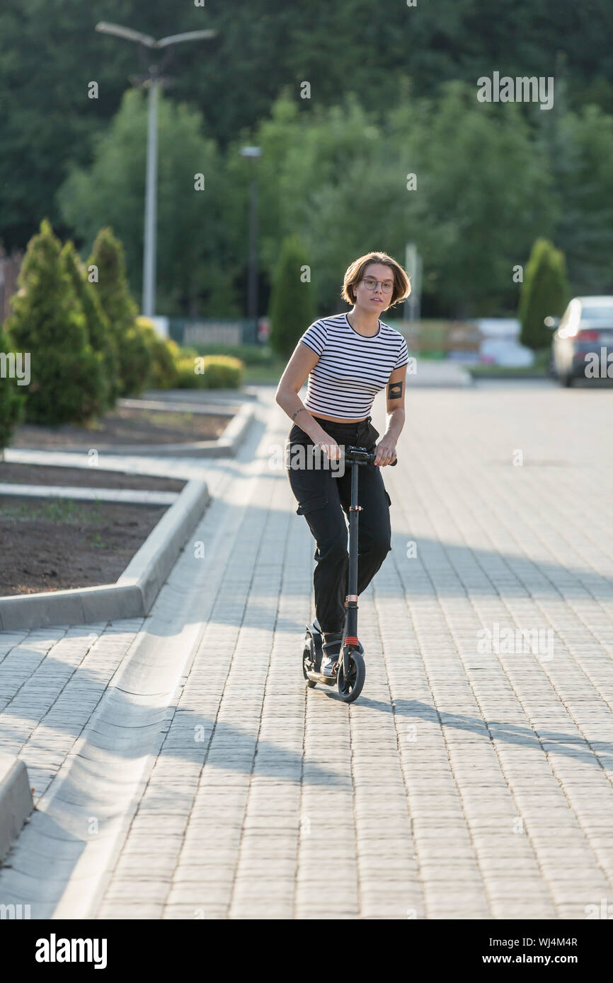 Young woman riding scooter push sur sunny road Banque D'Images