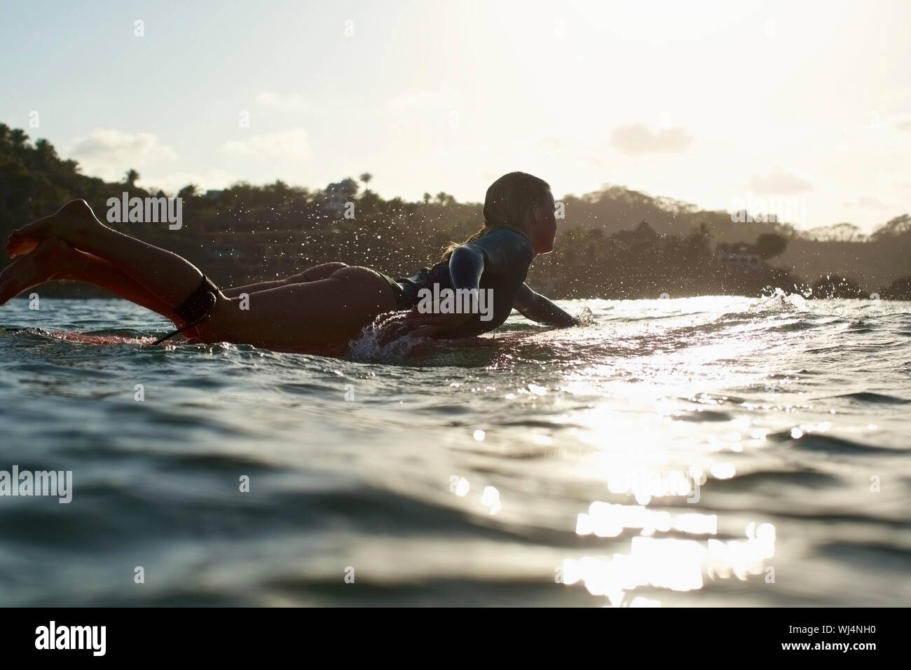 Silhouette femme surfer paddling out sur sunny, coucher soleil océan Banque D'Images