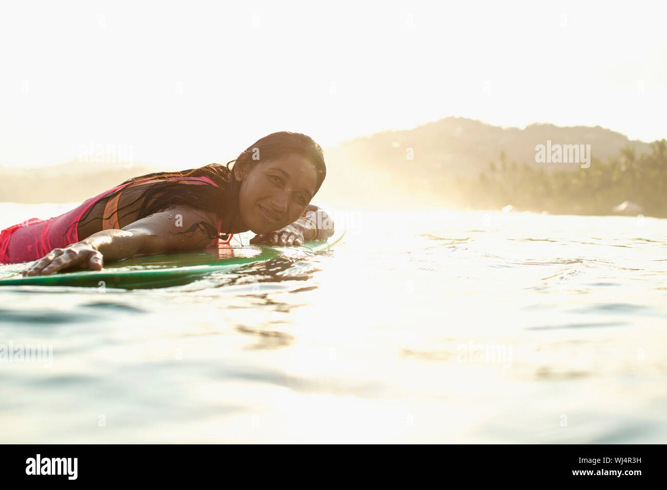 Portrait confiant, serein surfeur femelle portant sur une planche de surf dans l'océan ensoleillé Banque D'Images