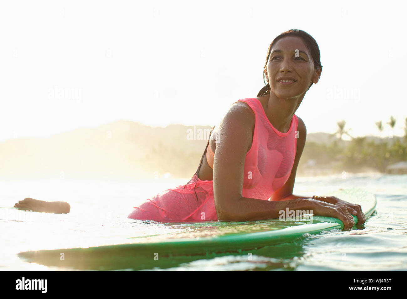 Confident female surfer appuyée sur une planche de surf dans l'océan ensoleillé Banque D'Images