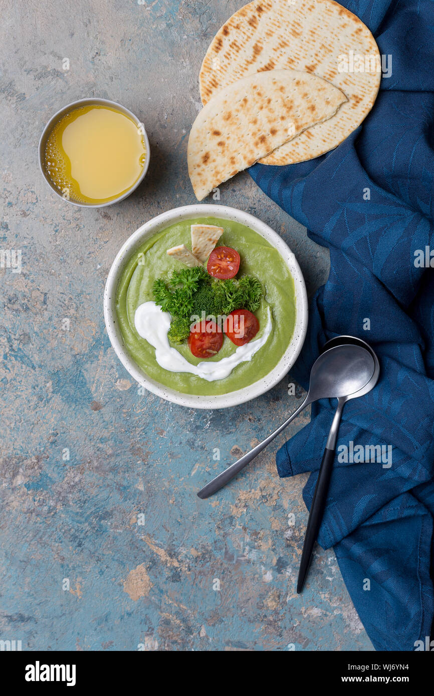 Soupe de crème verte avec la crème et le brocoli et les tomates sur le béton. Serviette bleu, cuillères, pita et près de jus d'orange. Concept de la cuisine de saison. Servant Banque D'Images Soupe de crème verte avec la crème et le brocoli et les tomates sur le béton. Serviette bleu, cuillères, pita et près de jus d'orange. Concept de la cuisine de saison. Servant Banque D'Images