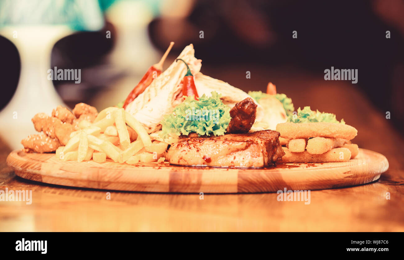 Les repas au restaurant. Planche de bois avec beaucoup de frites et bâtonnets de poisson viande burrito steak servi avec une salade. Menu snack-bar. Calories élevé pour le groupe d'amis. De délicieux en-cas savoureux. Snack pour la bière. Banque D'Images