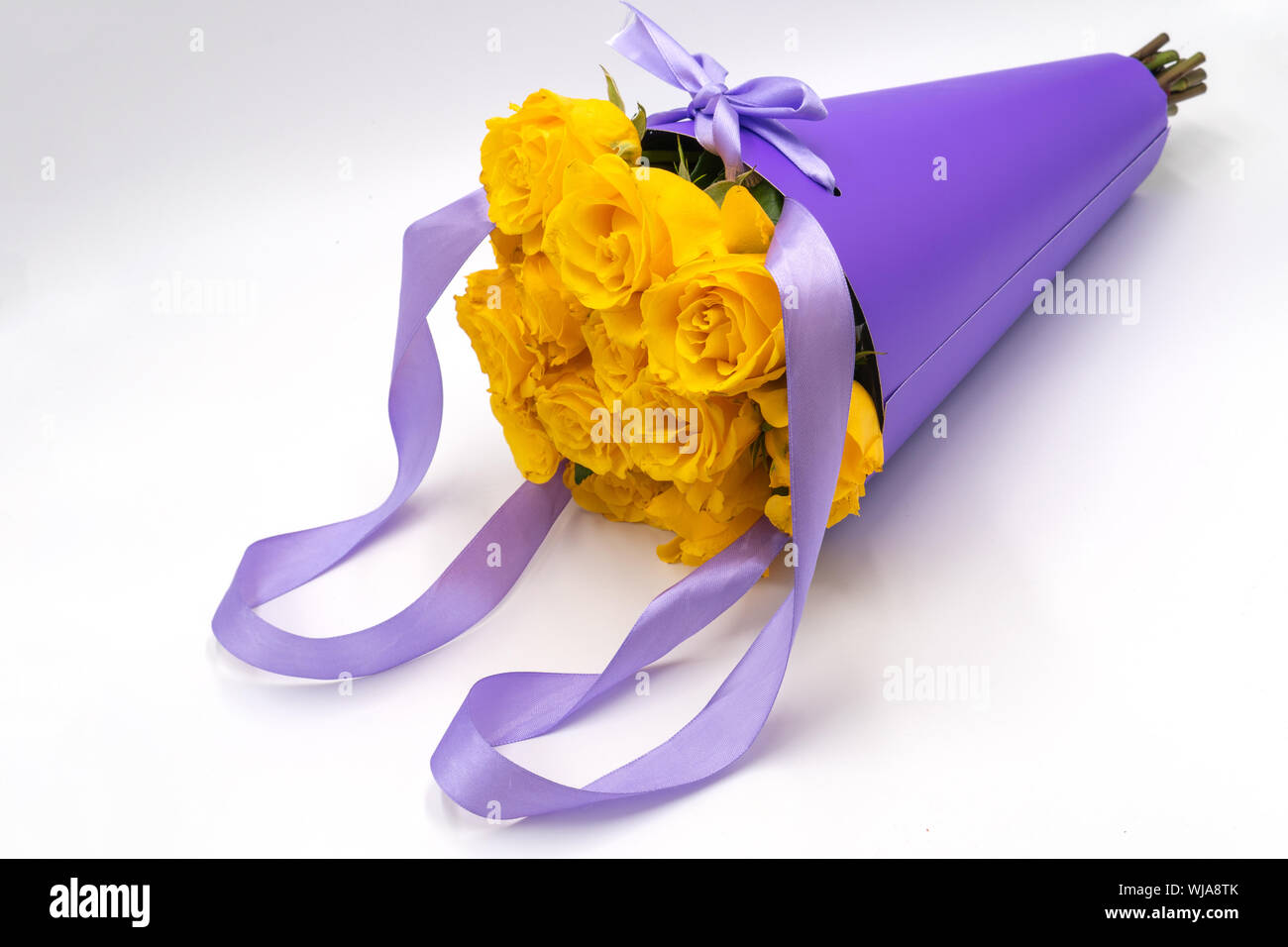 Un bouquet de roses jaunes dans un paquet élégant et moderne dans la forme d'un cône avec des poignées sur un fond blanc. La fête des mères et anniversaire. Banque D'Images