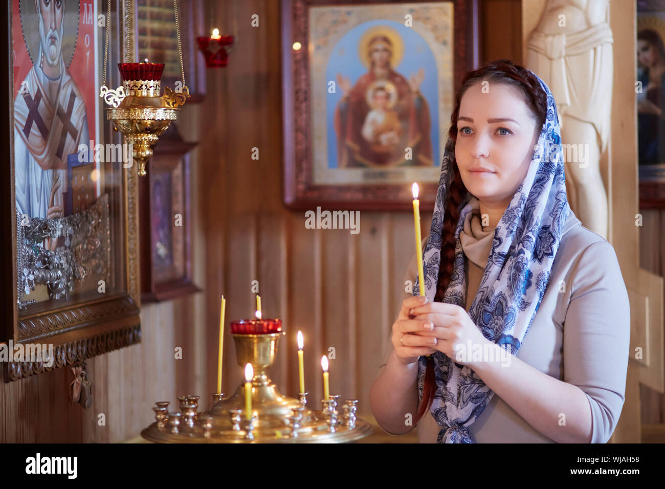 Femme dans l'Église orthodoxe russe avec les cheveux rouges et un foulard  sur sa tête s'allume une bougie et prie devant l'icône Photo Stock - Alamy