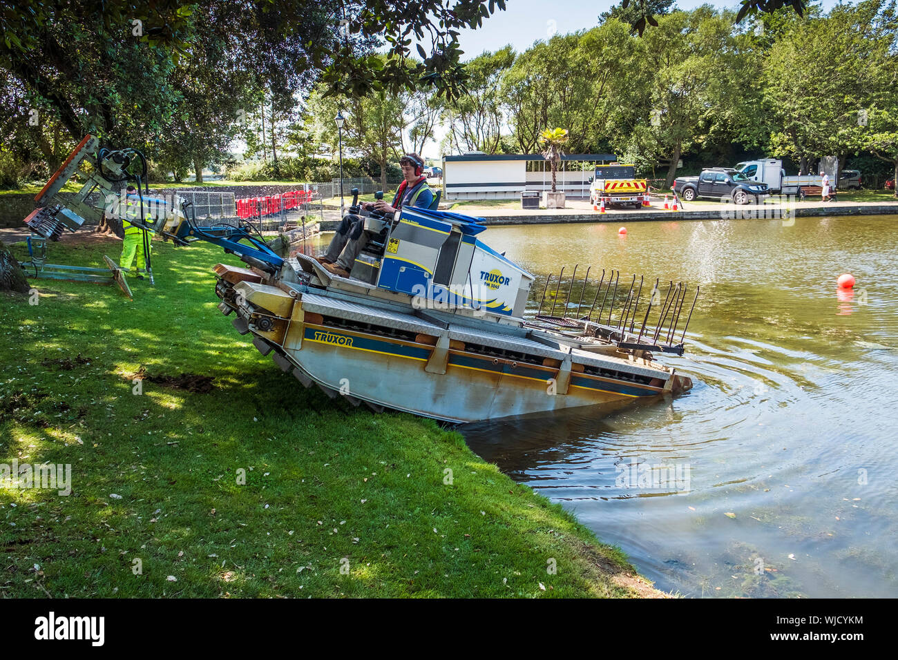 Un Truxor DM 5045 un automoteur amphibian toolcarrier avec précaution de recul pour travailler sur la lutte contre les mauvaises herbes envahissantes en Trenance lac de plaisance à Newquay Banque D'Images