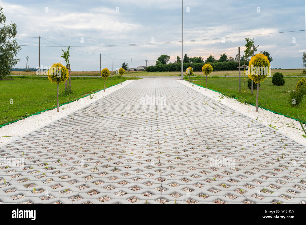 L'entrée pour les voitures dans les biens faits d'un revêtement en béton ajouré rempli de cailloux colorés, autour de est de l'herbe verte et les petits arbres. Banque D'Images