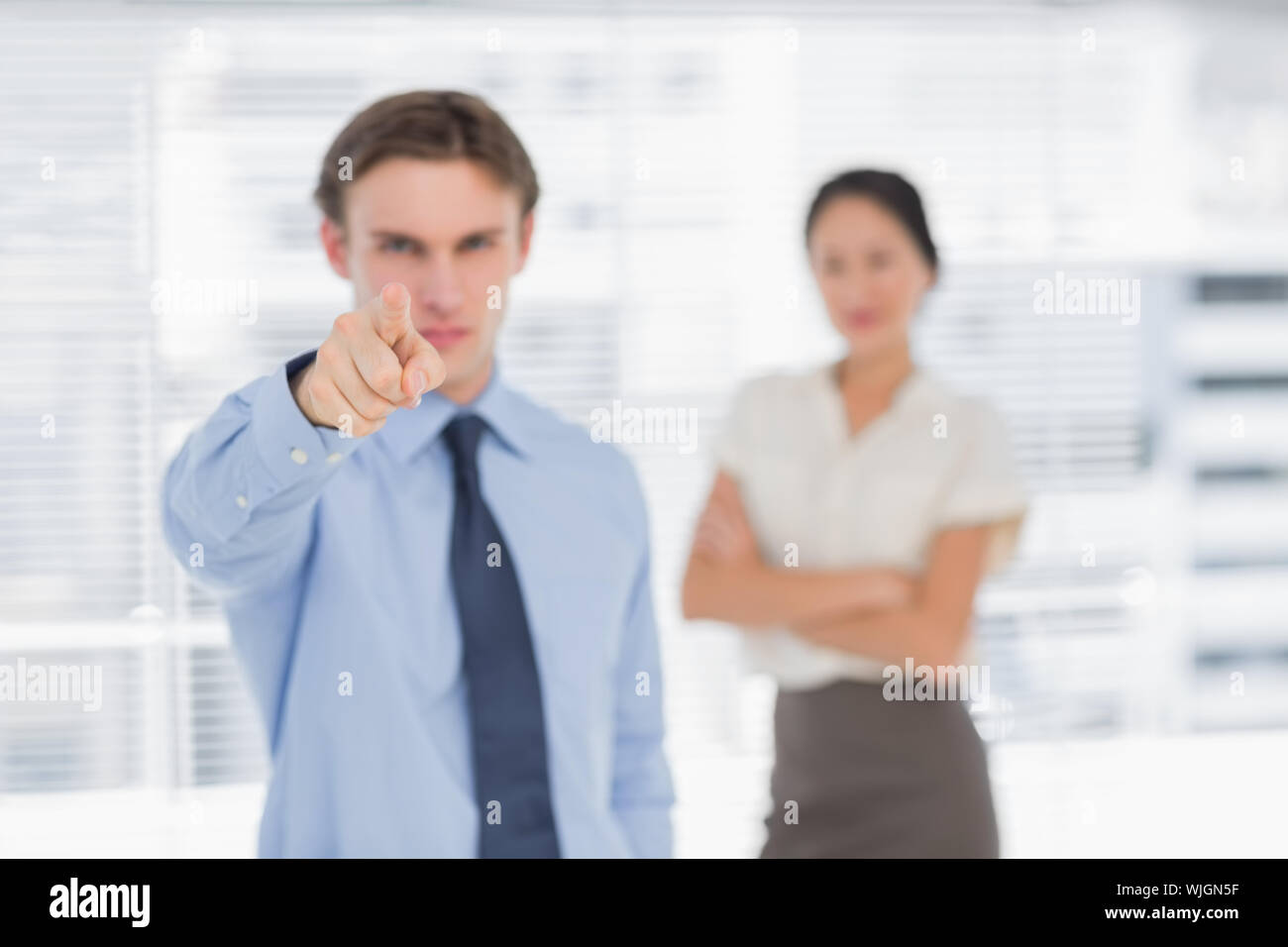 Portrait d'un homme pointant vers l'appareil photo avec la femme en arrière-plan au bureau Banque D'Images