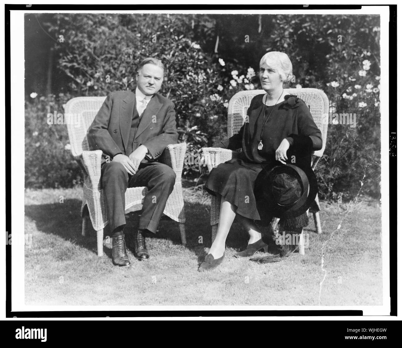 Herbert Hoover et Mme Hoover, portrait en pied, assis sur des chaises en osier, face à l'avant Banque D'Images