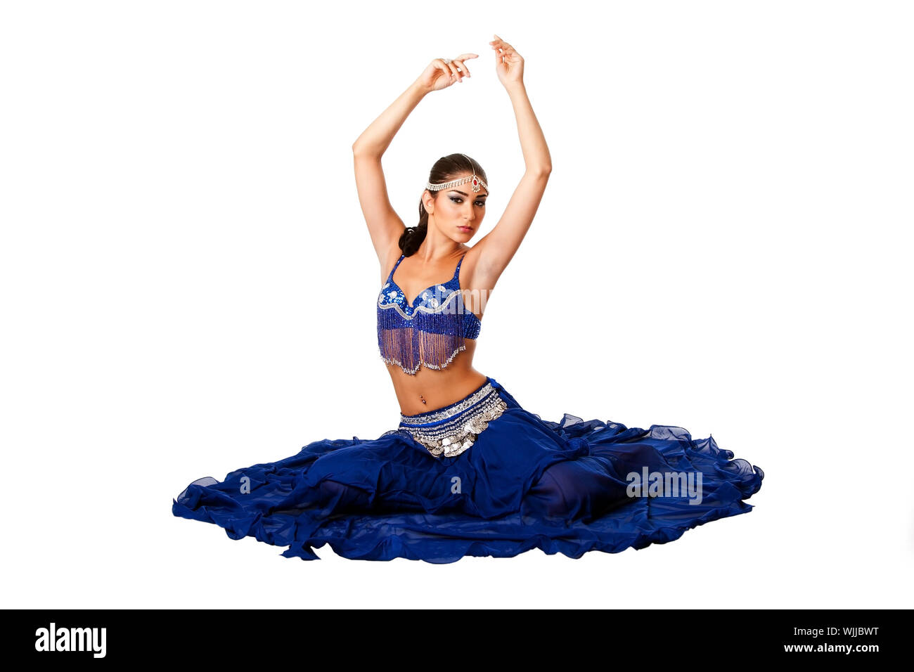 Belle égyptienne Israélien moyen-orientale danseuse du ventre libanaise performer en bleu jupe et soutien-gorge avec des bras dans l'air assis, isolé. Banque D'Images