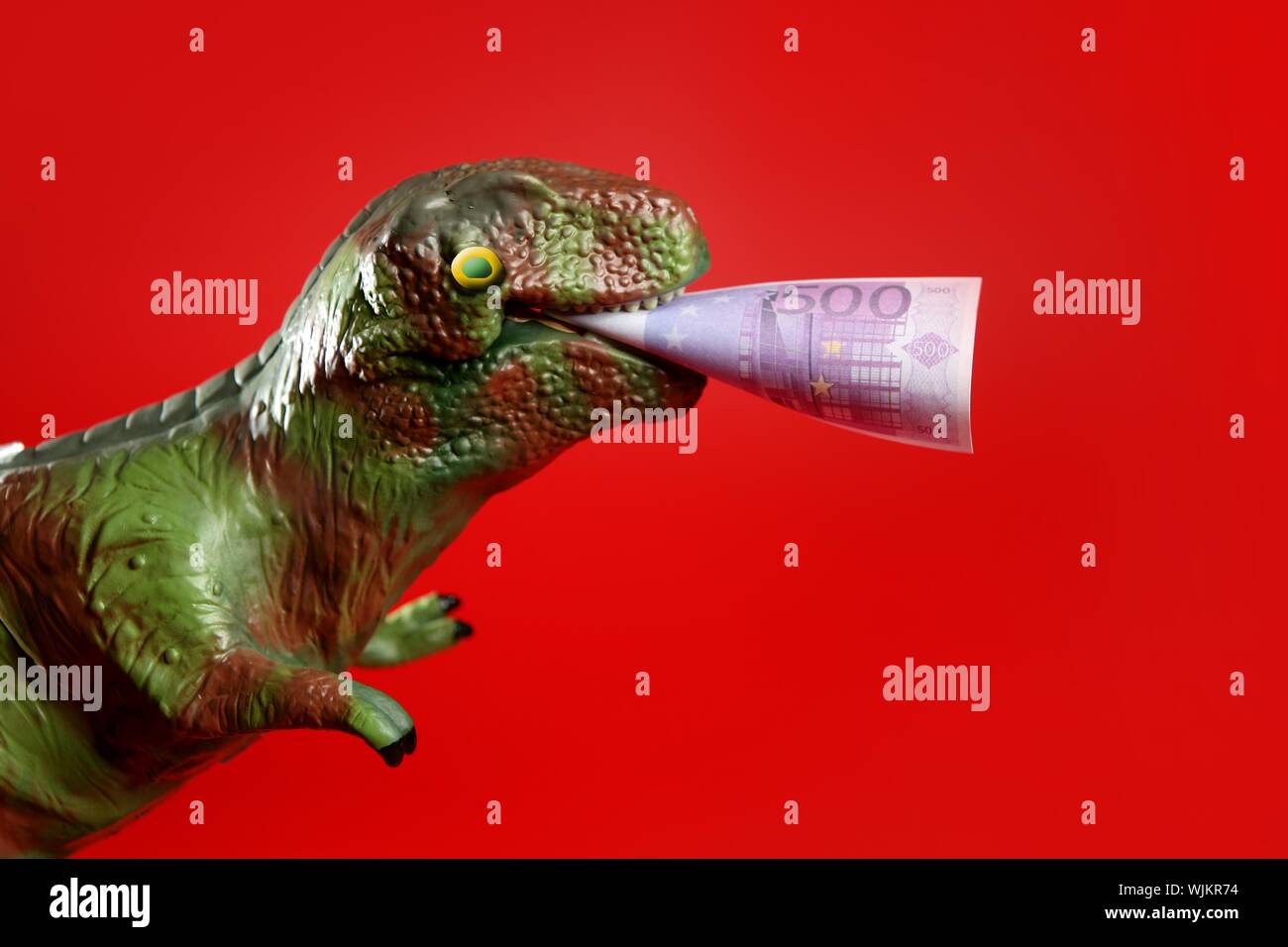 Dinosaure jouet avec euro note dans son pian sur fond rouge Banque D'Images