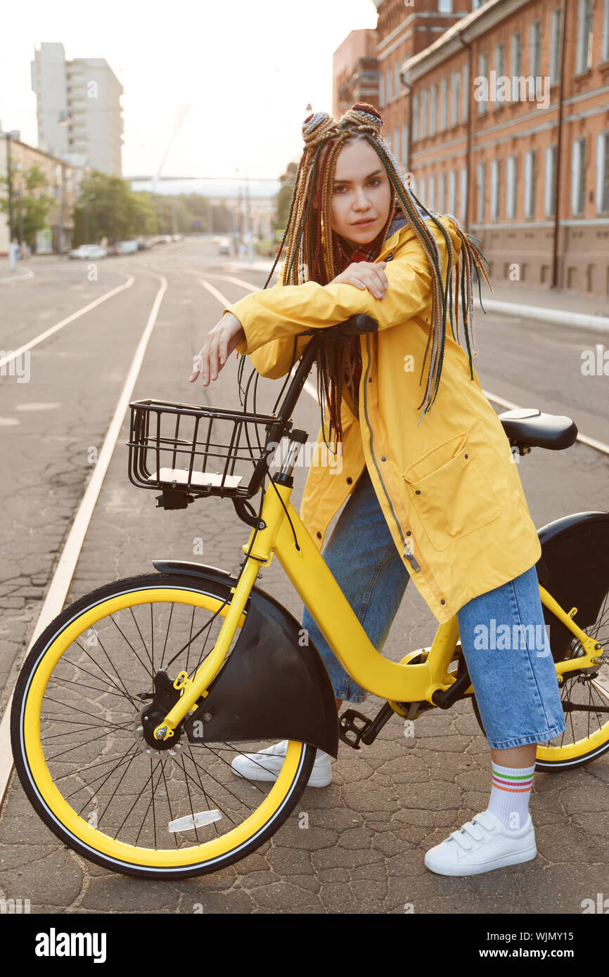 Jeune femme portant manteau de couleur jaune et des tresses, équitation,  vélo en ville Photo Stock - Alamy