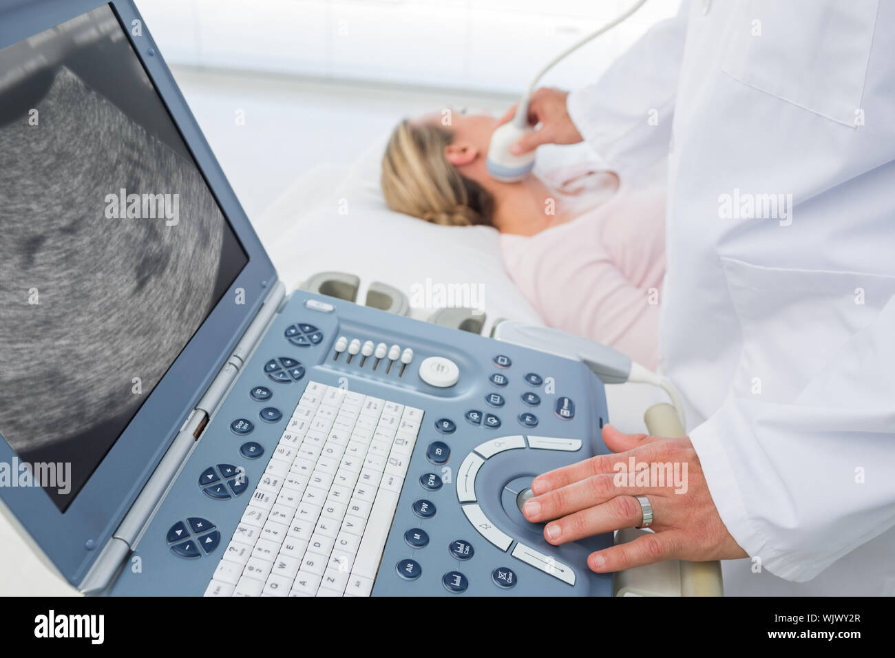 Médecin homme utilisant sonogramme sur le cou de female patient in examination room Banque D'Images