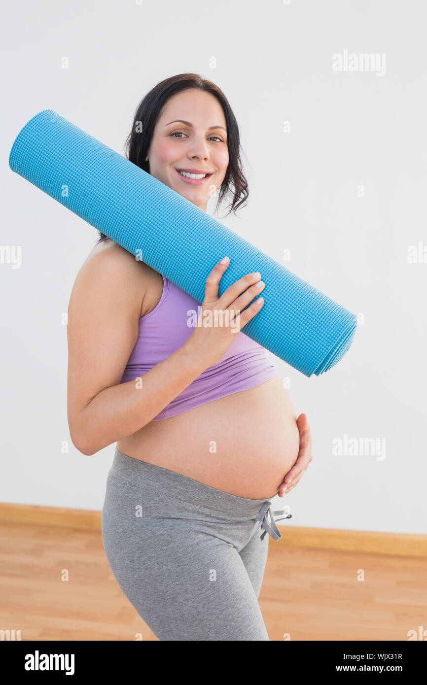 Pregnant woman holding exercise mat smiling at camera dans un studio de remise en forme Banque D'Images